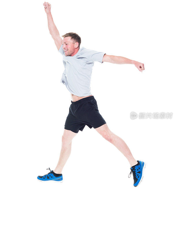 全长/一人/一人/侧视图20-29岁英俊的人棕色头发/短发高加索男性/年轻男子跳在白色背景下，穿着跑步短裤/短裤/运动鞋，双臂伸展